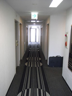 A hotel corridor with a striped carpet, doors on both sides, and a directional sign above the doors. - APA Hotel Tokushima-Ekimae (Tokushima)