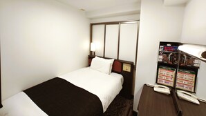 Hotellihuone, jossa on sänky, yöpöytä, lamppu ja ilmoitustaulu, jossa on informatiivisia julisteita.