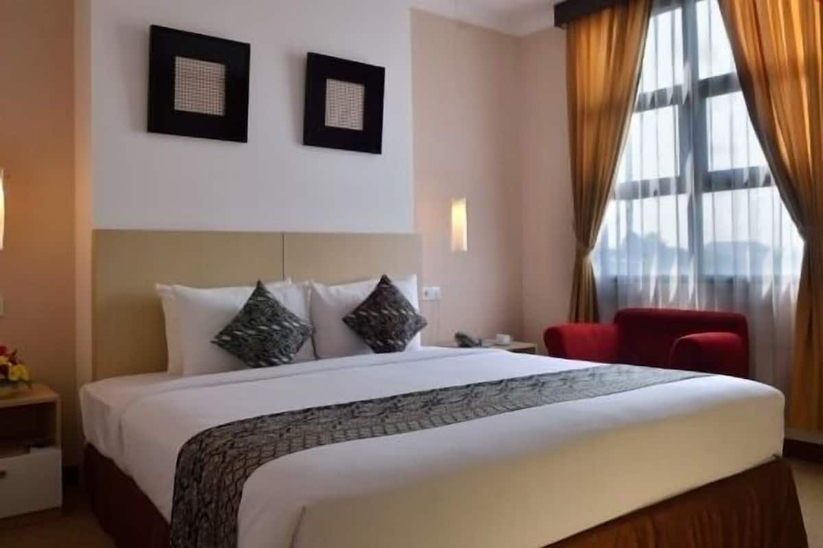 A hotel room with a large bed, two wall-mounted picture frames, a red chair, and a nightstand with a lamp.