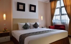Une chambre d’hôtel avec un grand lit, deux cadres photos accrochés au mur, une chaise rouge et une table de chevet avec une lampe.