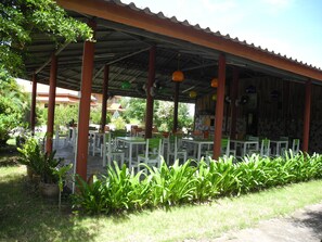 An outdoor seating area with tables and chairs, surrounded by greenery and a covered roof structure. - The Garden Resort Nongkhai (Nong Khai)