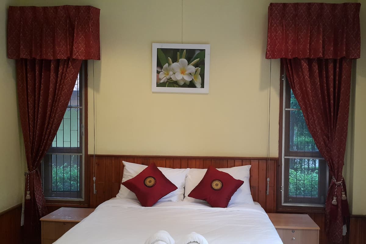 A hotel room with a large bed, two red pillows, a white headboard, and a framed picture on the wall.