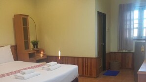 Una habitación de hotel con una cama, un armario de madera, una mesita con una planta, una puerta y una ventana con cortinas.