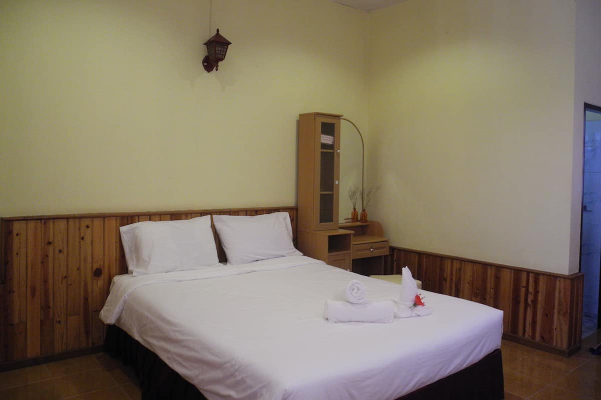 A hotel room with a wooden headboard, a bed with white linens, a wooden nightstand with a mirror, and a wooden cabinet.