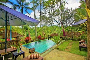 A pool area with a small waterfall, surrounded by lush greenery and palm trees.