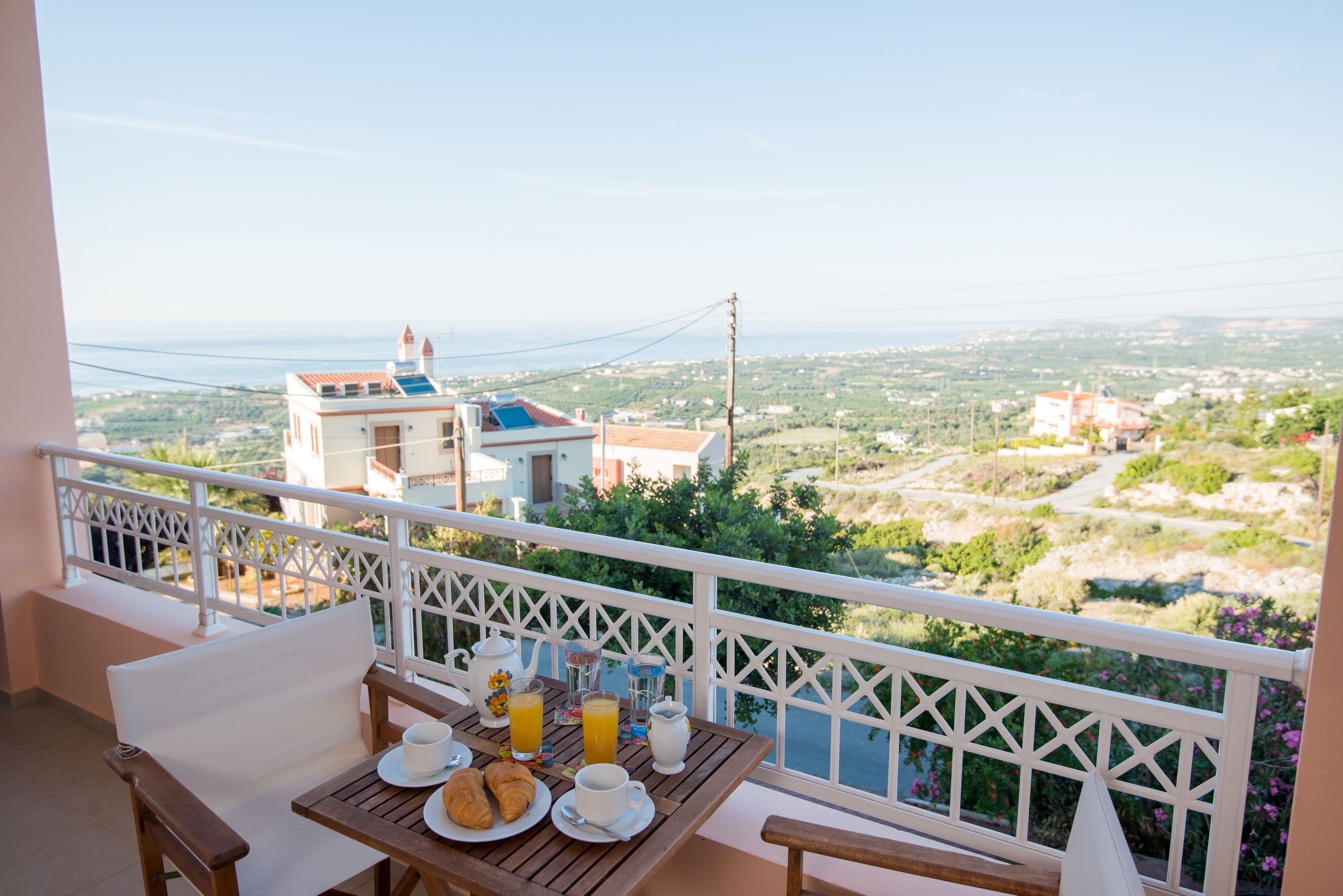 A balcony with a table set for breakfast, overlooking a scenic landscape with buildings and greenery.