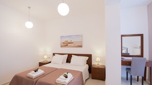 A hotel room with a double bed, two bedside tables with lamps, a desk with a chair, a large mirror, and a painting on the wall. - Diogenis Home (Rethymno)