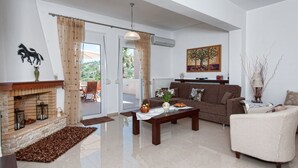 A modern living room with a fireplace, a sofa, a coffee table, and a dining area with chairs. - Diogenis Home (Rethymno)