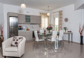 A modern kitchen with a stainless steel refrigerator, wooden cabinets, and a dining area with white chairs and a glass table.