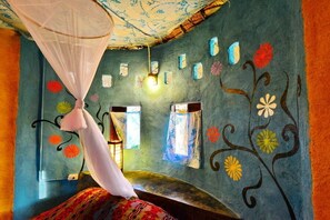 A room with a bed, a mosquito net, and walls decorated with floral patterns.
