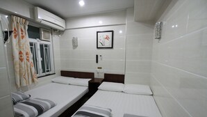 A hotel room with two single beds, a window with curtains, an air conditioning unit, and a framed picture on the wall. - Tai Wah Guest House (Kowloon)