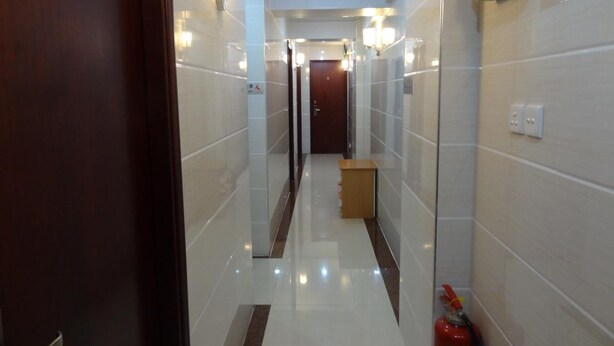 A hotel hallway with a wooden door on the left, a fire extinguisher on the right, and a wooden bench in the center. - Tai Wah Guest House (Kowloon)