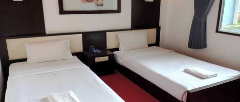 A hotel room with two single beds, a nightstand with a phone, a framed picture on the wall, and a window with curtains.