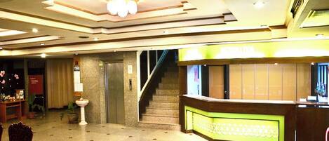 Eine Hotlellobby mit einer Rezeption, einer Treppe und einer Kronleuchter.