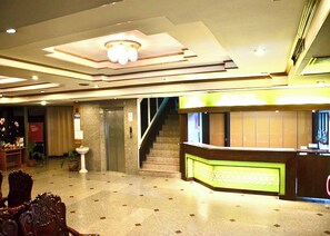 Un hall d’hôtel avec un comptoir d’accueil, un escalier et un lustre.