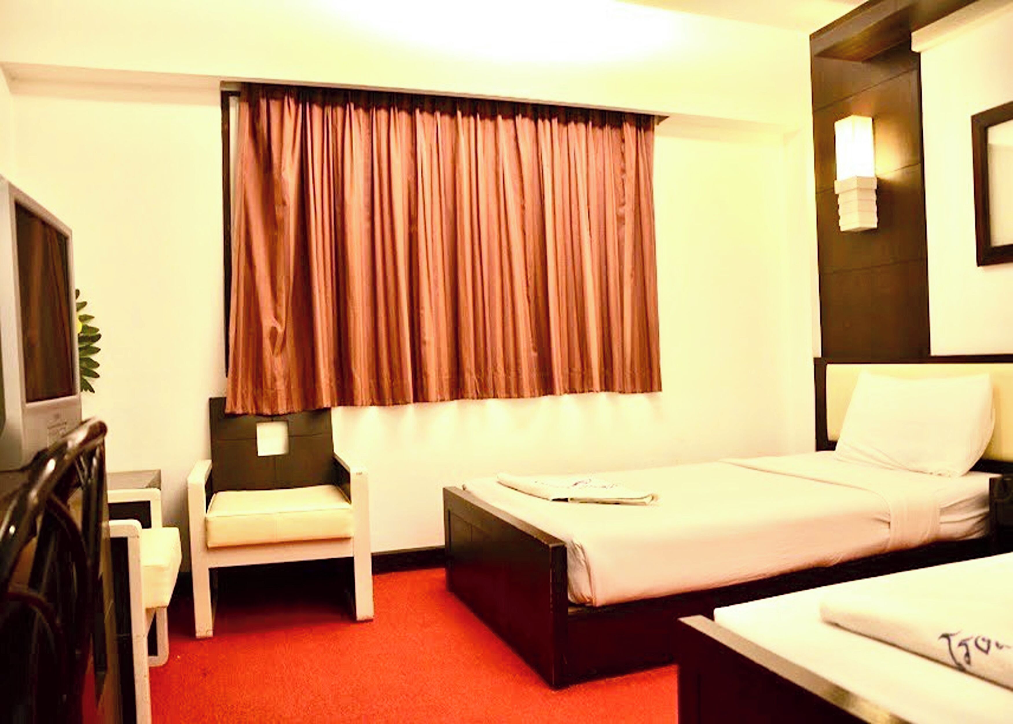 Une chambre d’hôtel avec un lit simple, un bureau, une chaise et une fenêtre avec des rideaux.