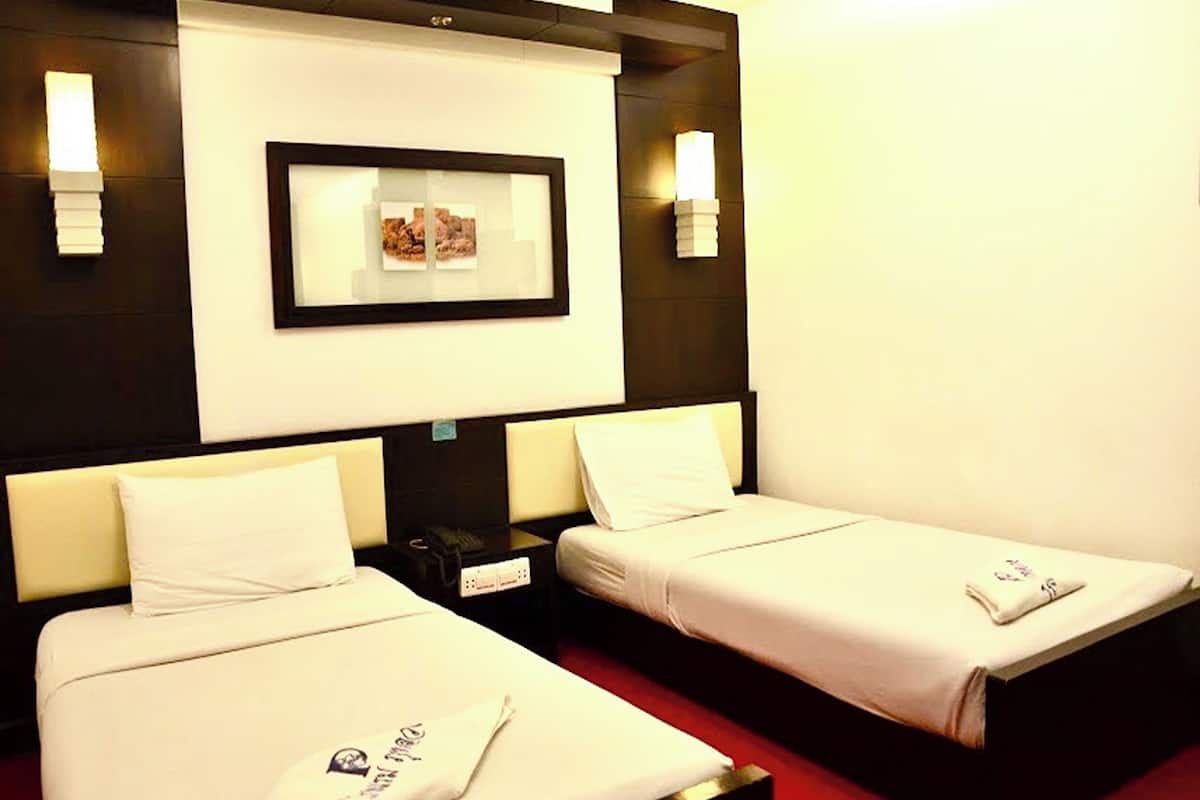 A hotel room with two single beds, a framed picture on the wall, and a small nightstand between the beds.