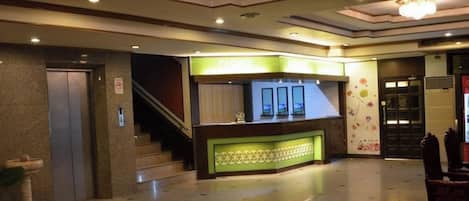 A hotel lobby with a reception desk, a staircase, and a door.