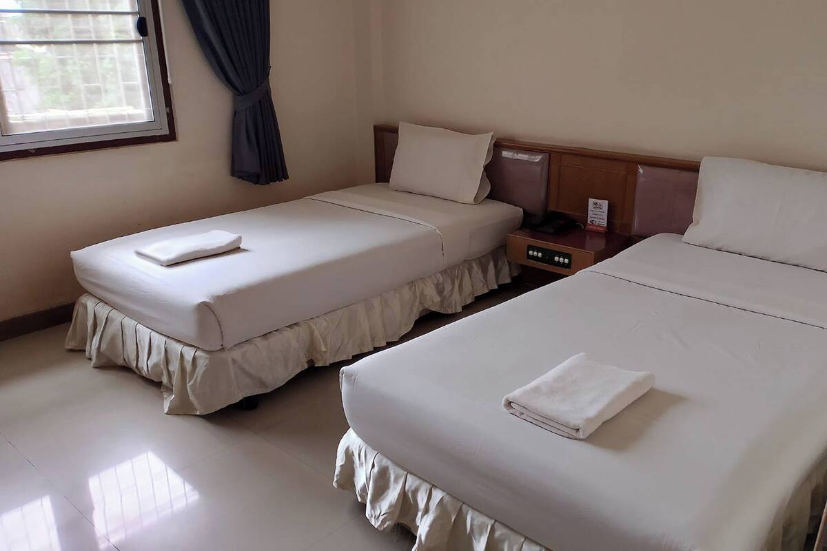 A hotel room with two single beds, a wooden headboard, a small bedside table with a phone and a sign, and a window with curtains.