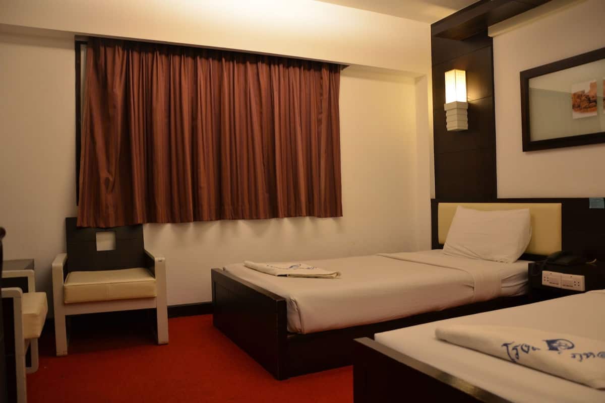 A hotel room with a bed, a desk, a chair, a window with curtains, a bedside lamp, and a framed picture on the wall.