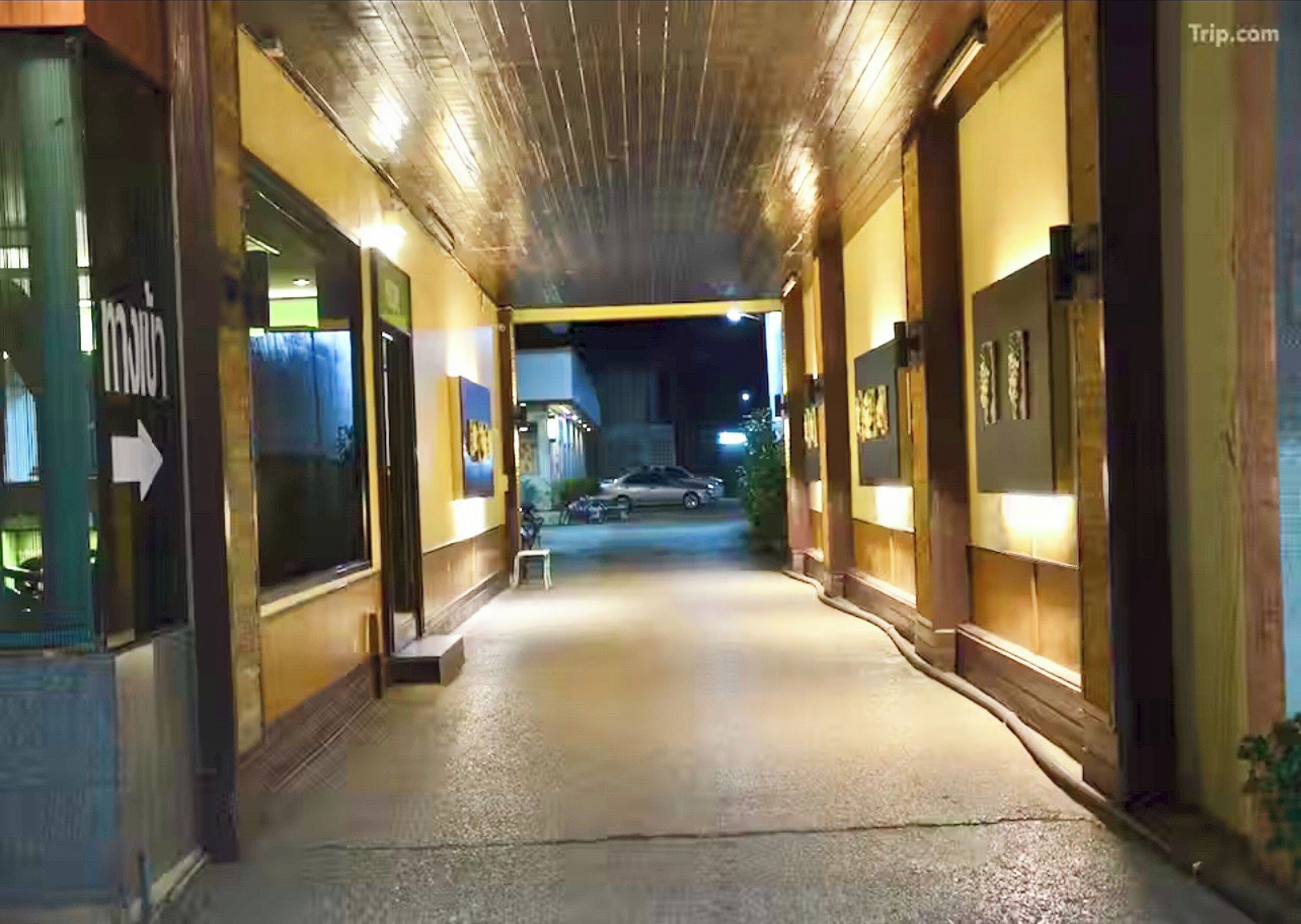 A corridor with a wooden ceiling, a bench, and a car parked outside.