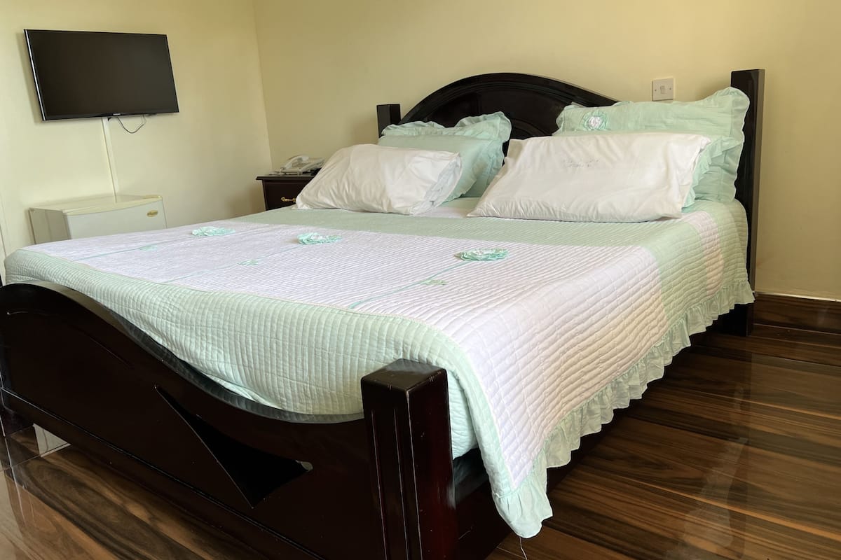 A neatly made bed with a quilted bedspread, a wooden headboard, and a bedside table with a lamp.