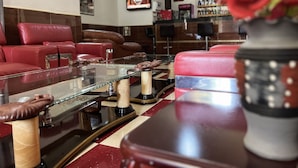 Una habitación con sofás de cuero rojo, una mesa de centro de vidrio con objetos decorativos, un televisor en la pared y una zona de bar con botellas.