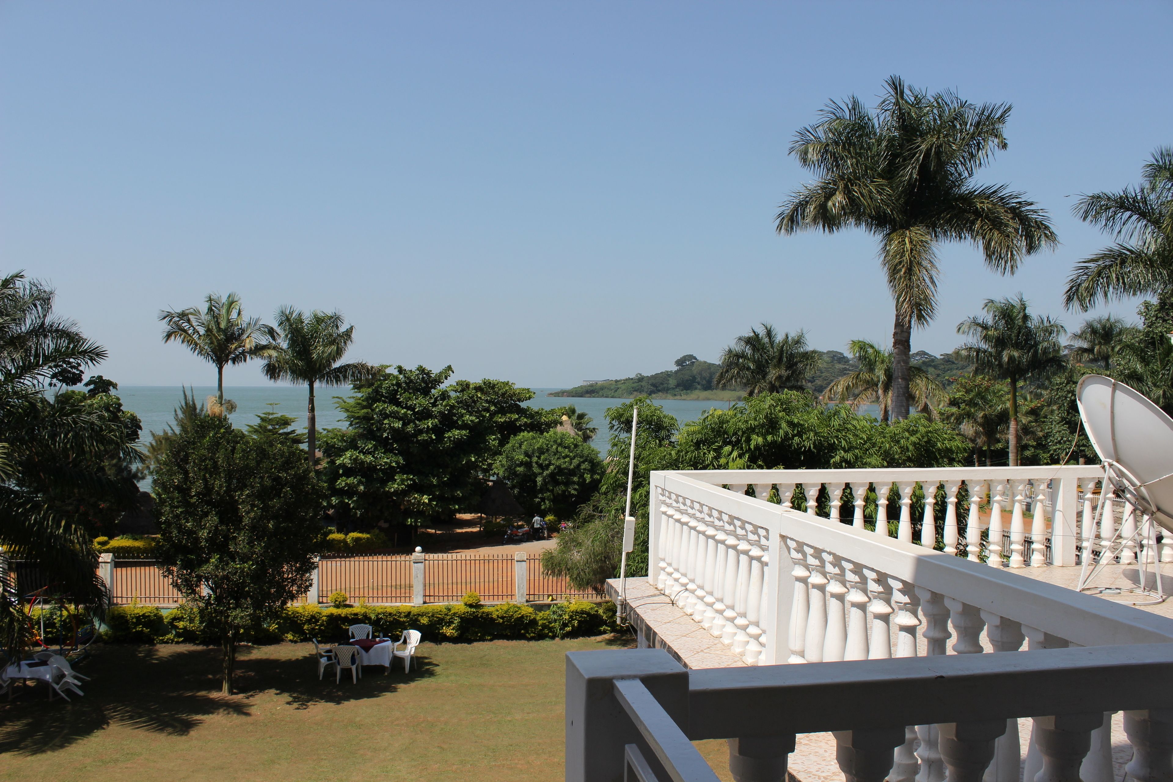 A balcony with a white balustrade overlooking a garden with palm trees and a view of the sea.