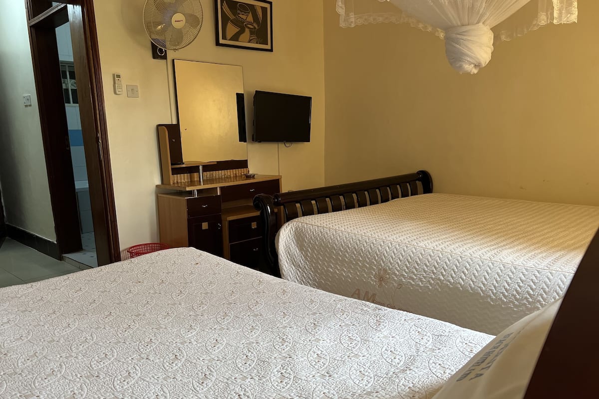 A bedroom with two beds, a desk, a chair, a mirror, a wall-mounted TV, and a ceiling fan.