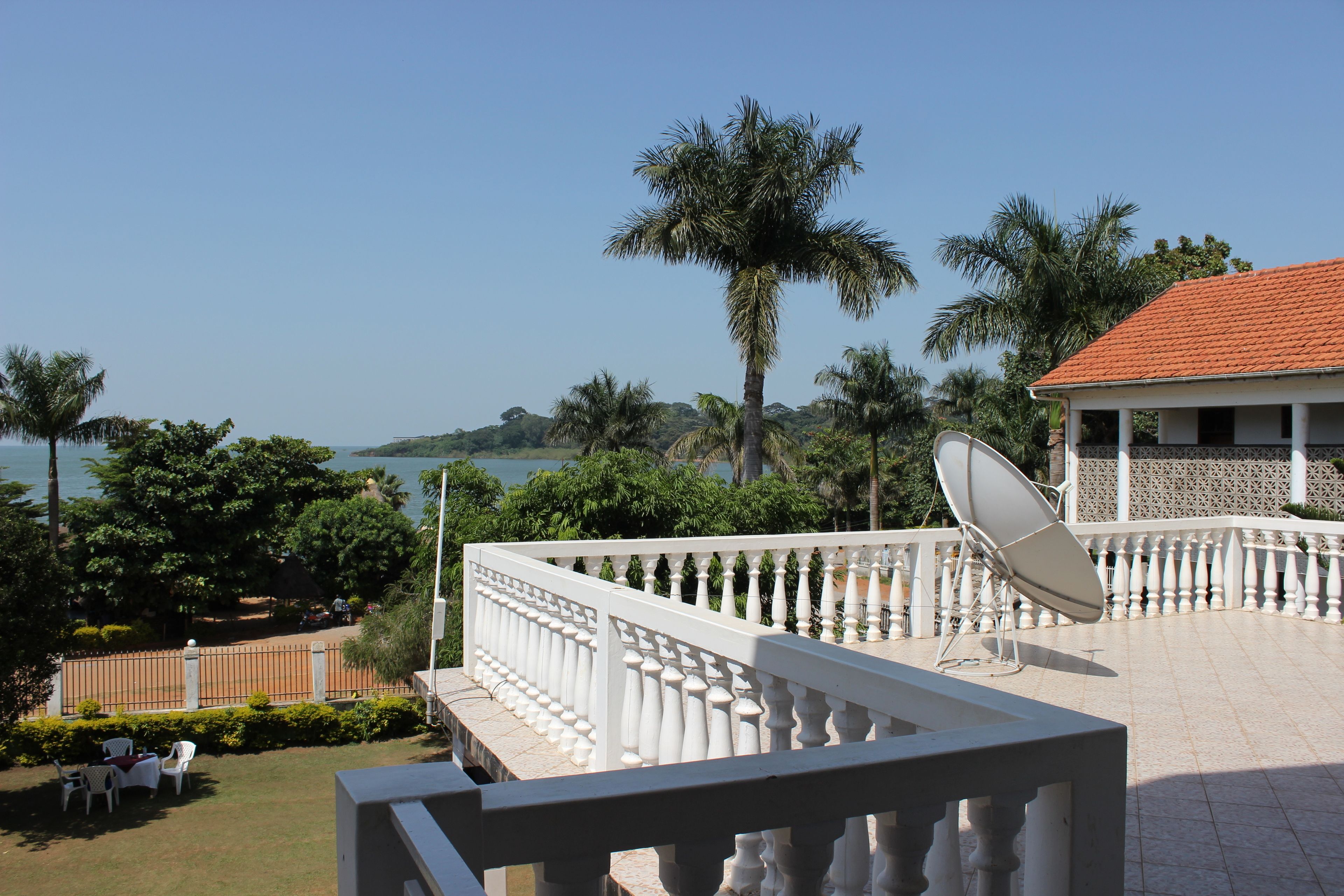 A balcony with a white railing, a satellite dish, and a view of the sea and palm trees.