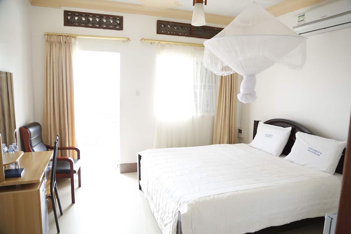 A hotel room with a bed, a desk, a chair, and a hanging mosquito net.