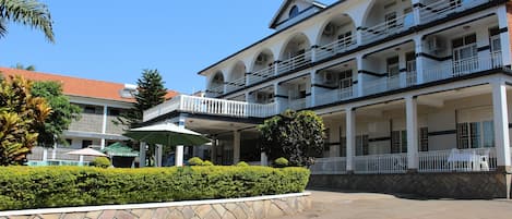 A multi-story building with balconies, a stone wall, and a well-maintained garden.
