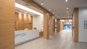Zona de recepció amb taulell de recepció, panells de fusta, un rellotge i un passadís que condueix a altres espais.