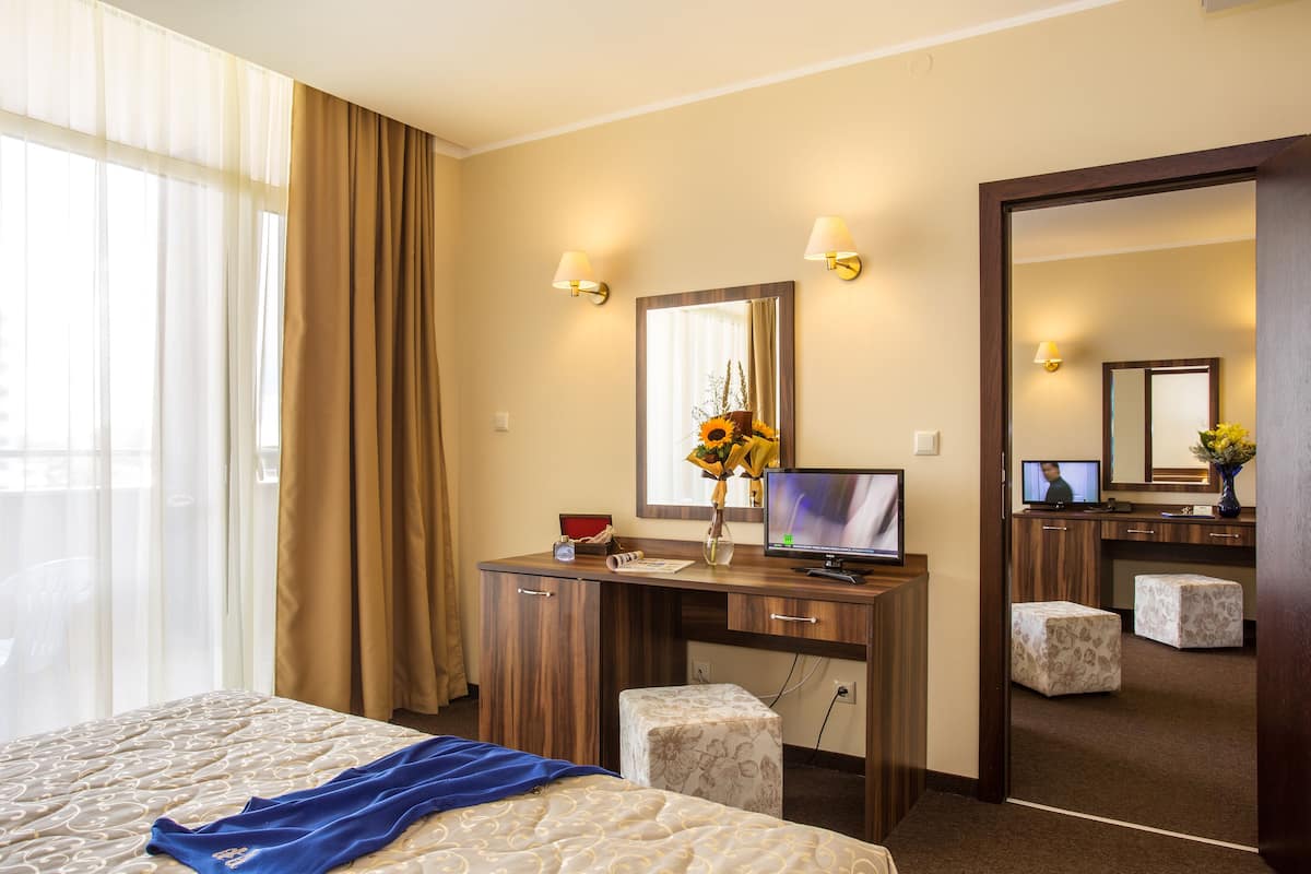 Une chambre d’hôtel avec un lit, un bureau avec un ordinateur, un miroir et une fenêtre avec des rideaux.