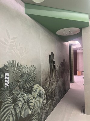 A hallway with a mural of tropical foliage, a green ceiling, and a modern light fixture.