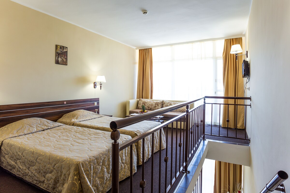 A hotel room with two beds, a balcony, a lamp, and a painting on the wall.