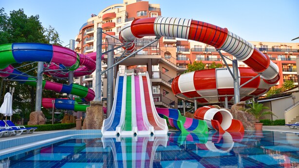 Una piscina amb diverses tobogans aquàtics de colors i un edifici amb balcons al fons.