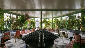 Een eetruimte met ronde tafels, een zwarte lederen zithoek en groene planten.