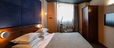 A hotel room with a large bed, a ceiling fan, a desk with a chair, and a TV mounted on the wall.