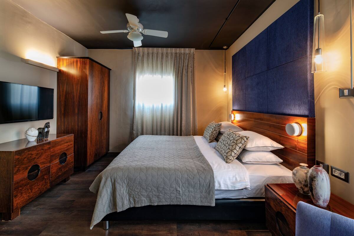 Una habitación de hotel moderna con una cama grande, un televisor de pantalla plana, un armario de madera y un ventilador de techo.