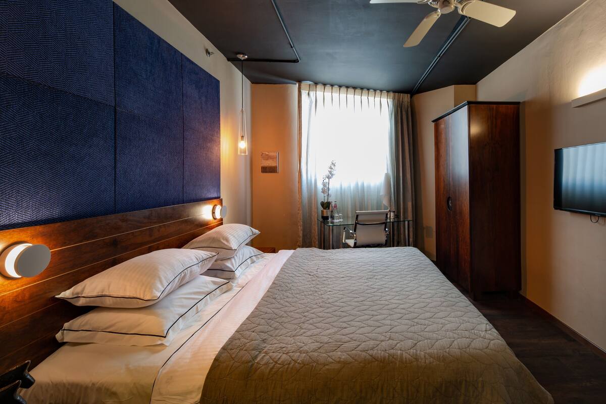 Una habitación de hotel con una cama grande, ventilador de techo, televisión, escritorio con silla y armario.