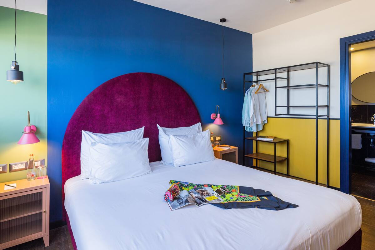 Una habitación de hotel moderna con una cama grande, un tocador con espejo y una mesita de noche con lámpara.
