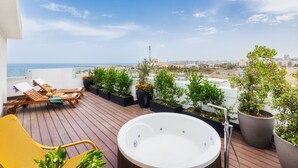 Een terras op het dak met een jacuzzi, lounge stoelen en plantenpotten.