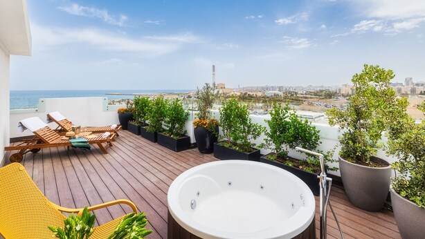 Een terras op het dak met een jacuzzi, lounge stoelen en plantenpotten.
