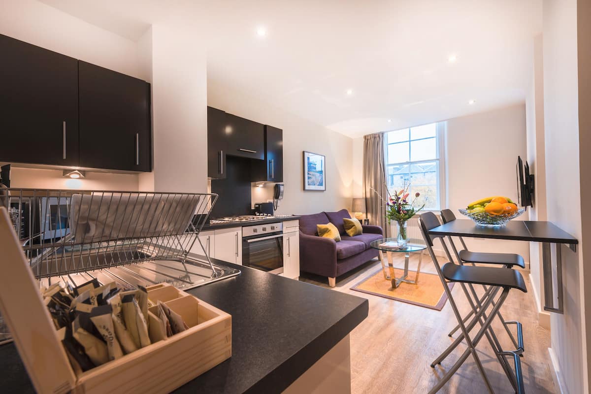 A modern kitchen with dark cabinets, a dining area with a table and chairs, and a sofa.