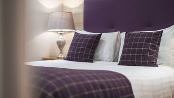 A neatly made bed with a purple headboard and two matching pillows, a bedside lamp, and a plaid-patterned blanket.
