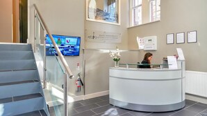 Un espace d’accueil avec un bureau en verre, un extincteur et un téléviseur diffusant des images d’un paysage urbain.