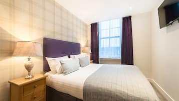 A hotel room with a bed, nightstands, a TV, and a window with curtains.