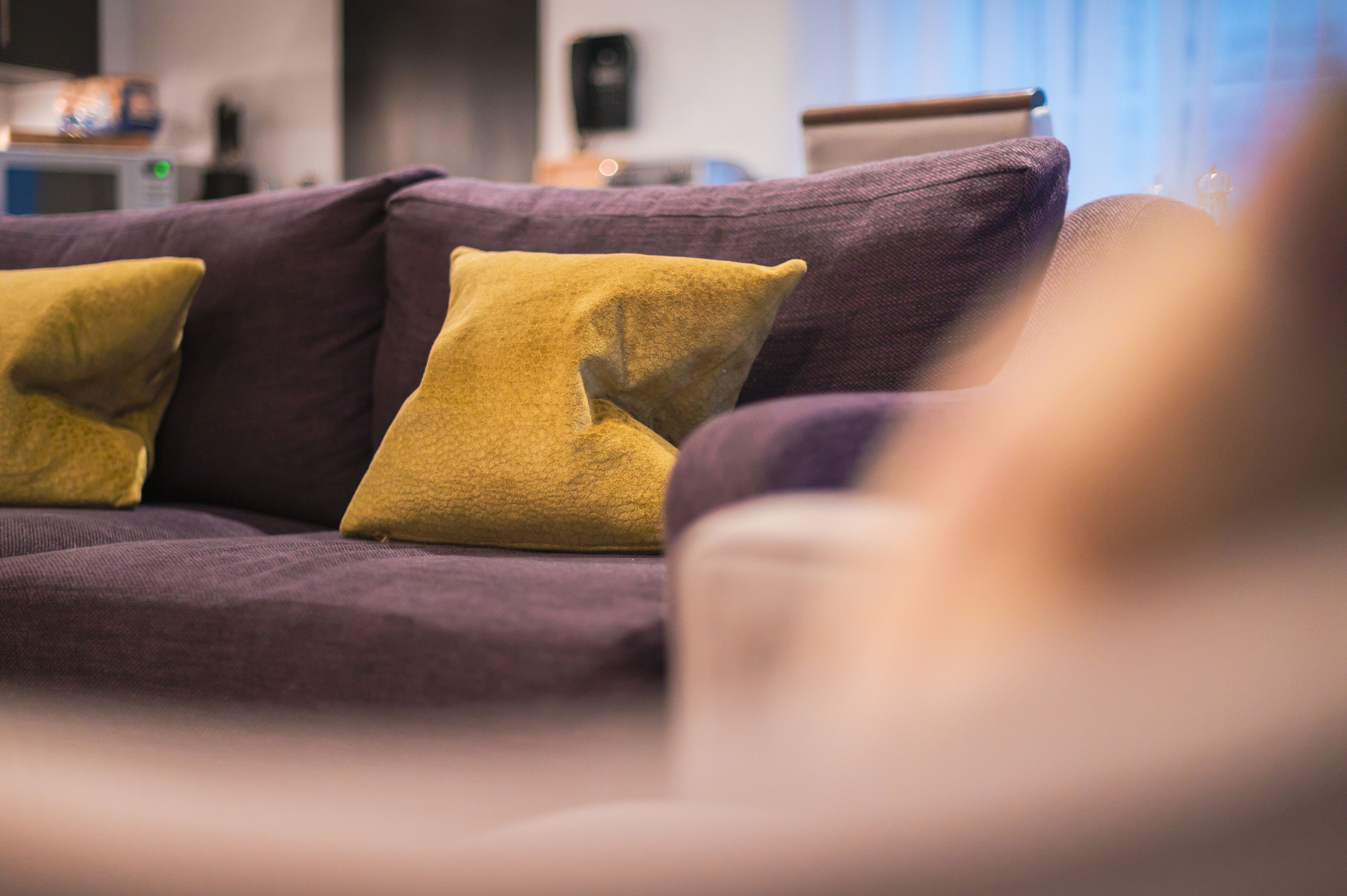 A purple sofa with two yellow cushions in a room with a blurred background.