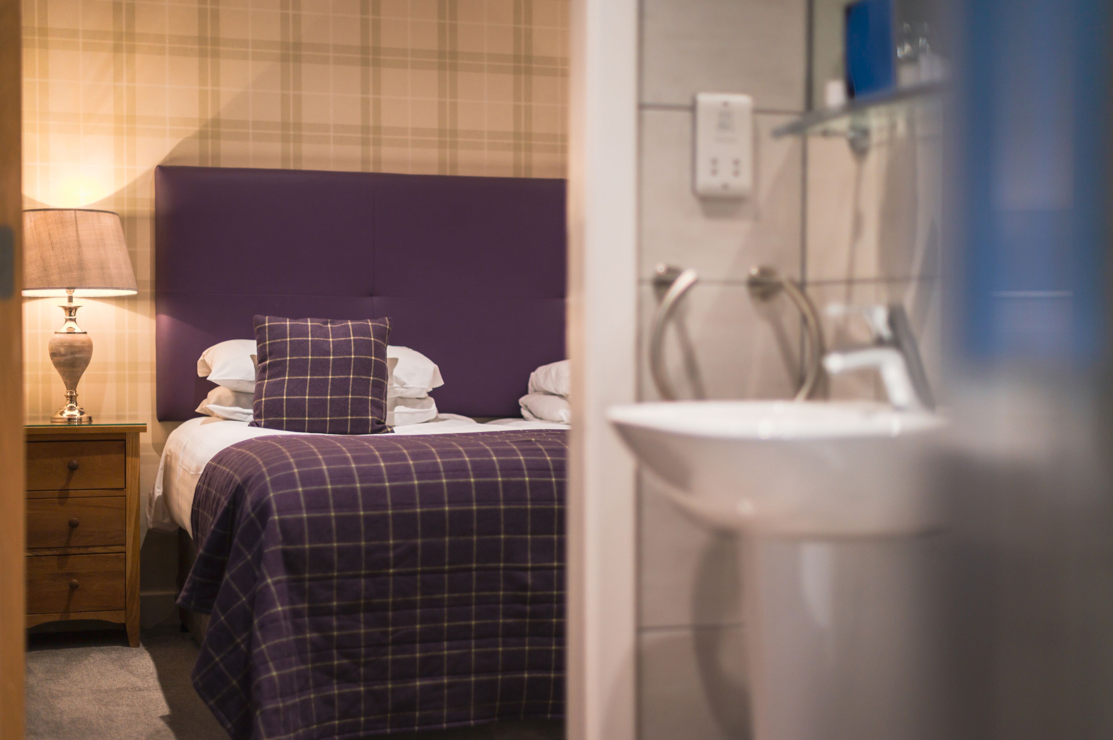 Ein Hotelzimmer mit Bett, Nachttisch mit Lampe und Badezimmer mit Waschbecken und Dusche.